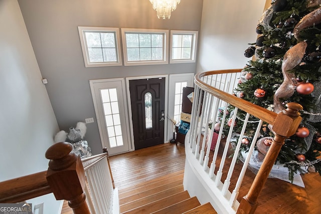 foyer entrance featuring hardwood / wood-style floors, a towering ceiling, and an inviting chandelier