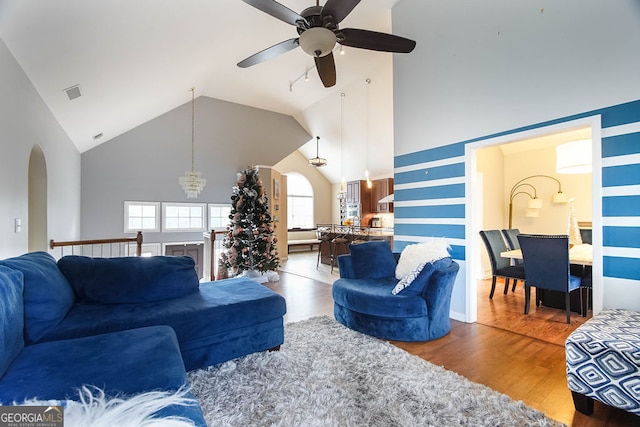 living room with wood-type flooring, ceiling fan with notable chandelier, and high vaulted ceiling