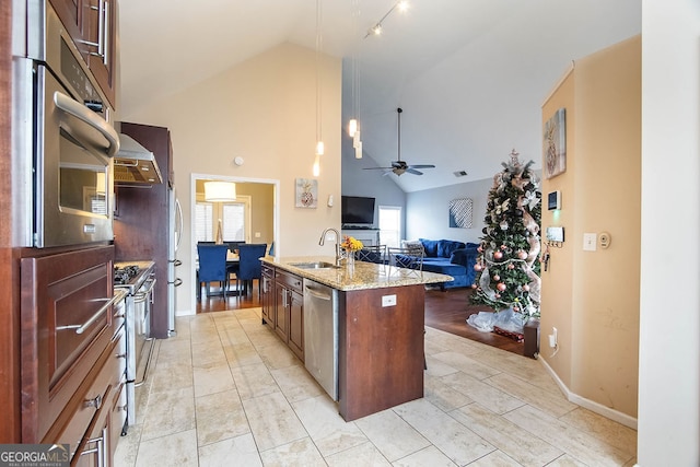 kitchen featuring light stone counters, stainless steel appliances, ceiling fan, sink, and an island with sink