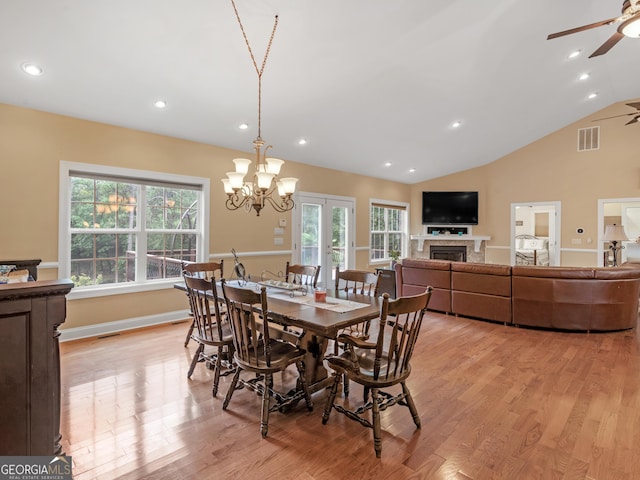 dining area with ceiling fan with notable chandelier, light wood-type flooring, a wealth of natural light, and vaulted ceiling