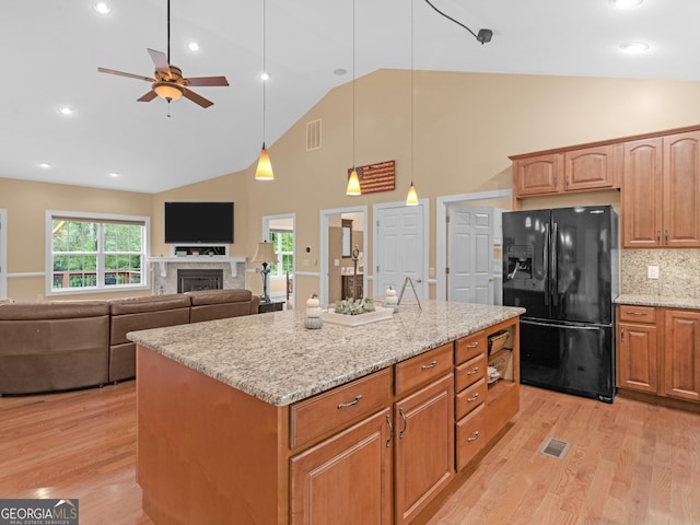 kitchen featuring backsplash, black fridge, light stone counters, ceiling fan, and a center island