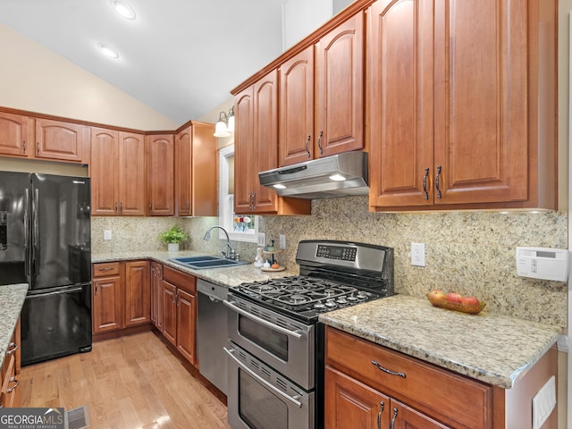 kitchen with sink, vaulted ceiling, light wood-type flooring, light stone countertops, and appliances with stainless steel finishes