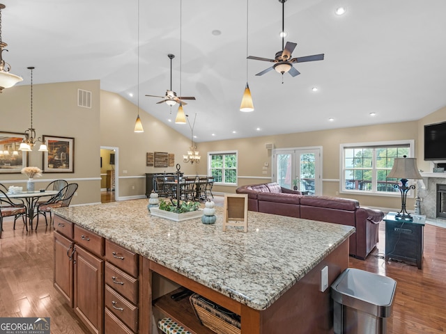 kitchen with a large island, light stone counters, pendant lighting, ceiling fan with notable chandelier, and hardwood / wood-style flooring