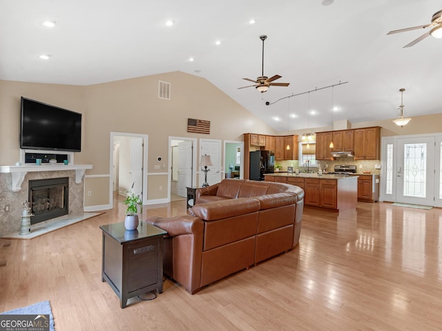 living room featuring ceiling fan, sink, high vaulted ceiling, light hardwood / wood-style flooring, and a fireplace