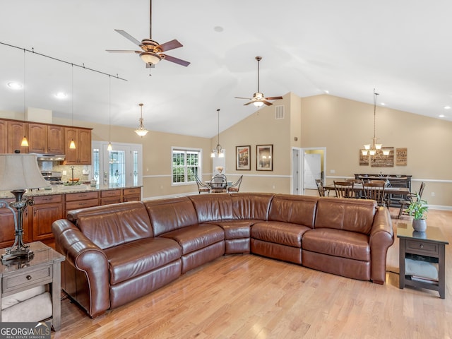 living room with vaulted ceiling, light hardwood / wood-style floors, and ceiling fan with notable chandelier