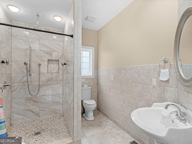 bathroom with tile patterned floors, sink, toilet, tile walls, and a tile shower