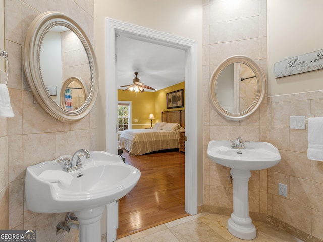 bathroom featuring ceiling fan, tile patterned flooring, dual sinks, and tile walls