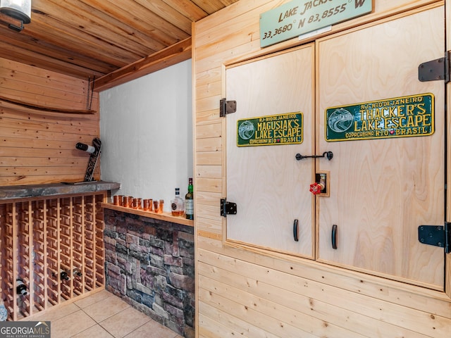 wine area featuring light tile patterned floors, indoor bar, wooden walls, and wood ceiling