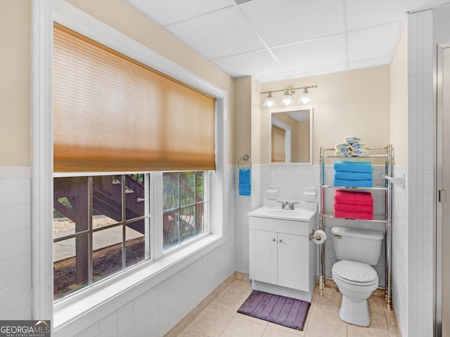 bathroom featuring tile patterned floors, a drop ceiling, vanity, tile walls, and toilet