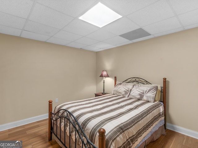 bedroom featuring a drop ceiling and light hardwood / wood-style flooring