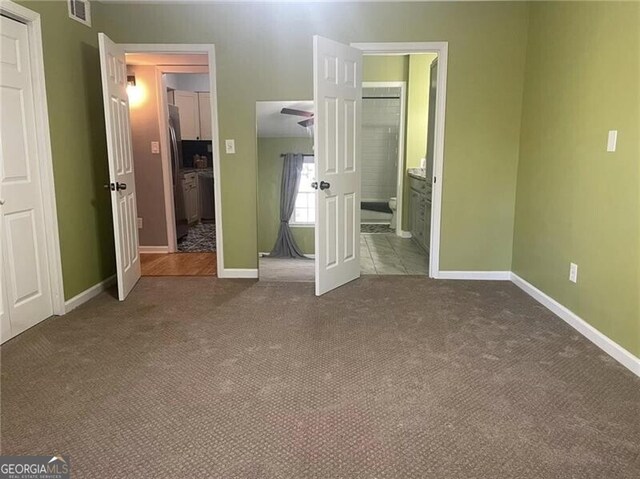 unfurnished bedroom with carpet, ensuite bathroom, and stainless steel refrigerator