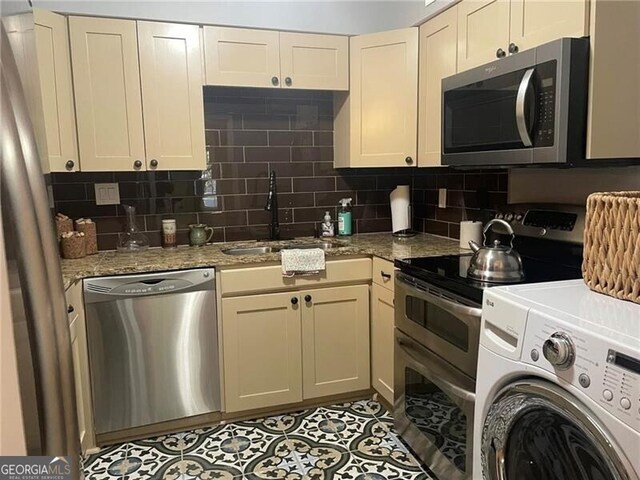 kitchen with washer / dryer, sink, cream cabinetry, and appliances with stainless steel finishes