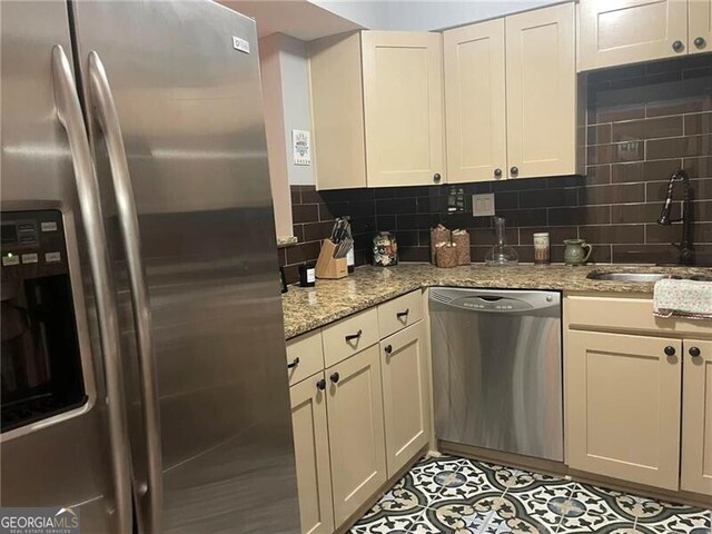 kitchen with cream cabinets, sink, decorative backsplash, light stone countertops, and appliances with stainless steel finishes