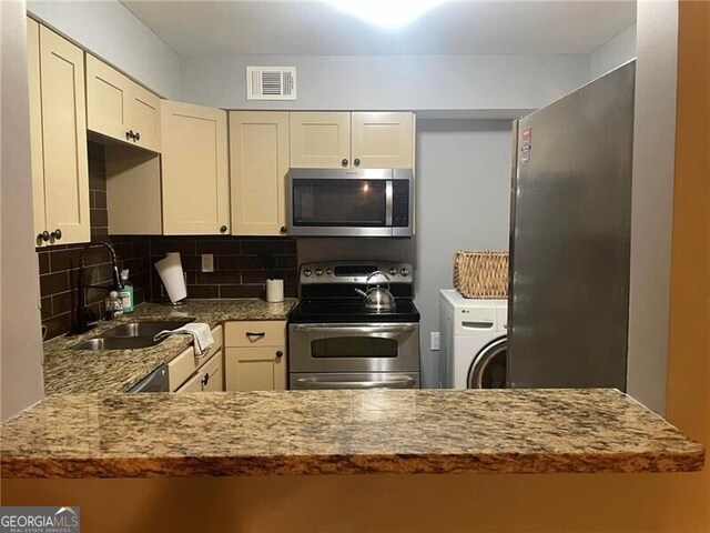 kitchen with light stone countertops, appliances with stainless steel finishes, decorative backsplash, sink, and washer / dryer