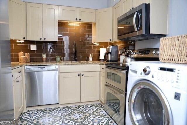 kitchen with washer / dryer, decorative backsplash, light stone countertops, and appliances with stainless steel finishes