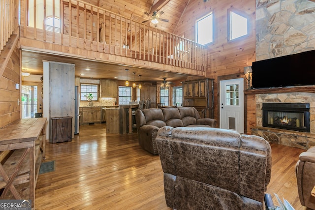 living room featuring ceiling fan, high vaulted ceiling, light wood-type flooring, a fireplace, and wooden walls