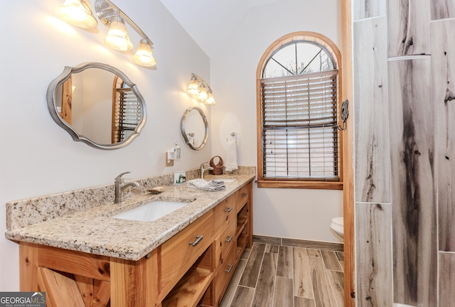 full bath with double vanity, wood tiled floors, toilet, vaulted ceiling, and baseboards