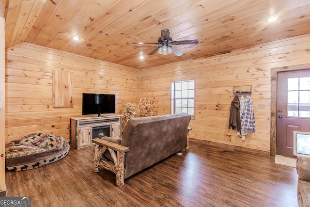 living area featuring wood ceiling, a ceiling fan, wood finished floors, a lit fireplace, and wooden walls