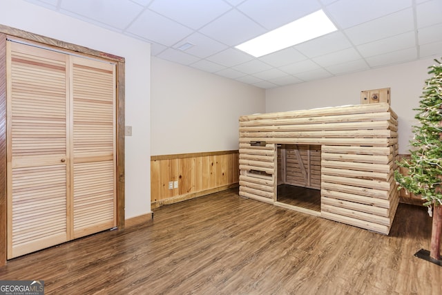unfurnished living room with a drop ceiling, wood finished floors, a wainscoted wall, and wooden walls
