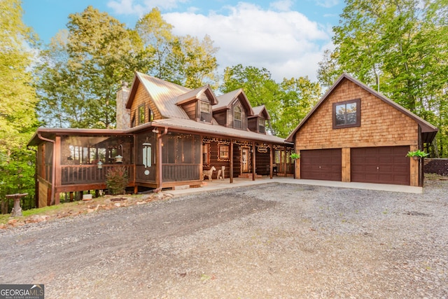 chalet / cabin with a chimney, a sunroom, a detached garage, an outbuilding, and metal roof