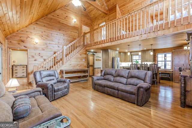 living area with stairs, wooden ceiling, wood walls, light wood-type flooring, and high vaulted ceiling