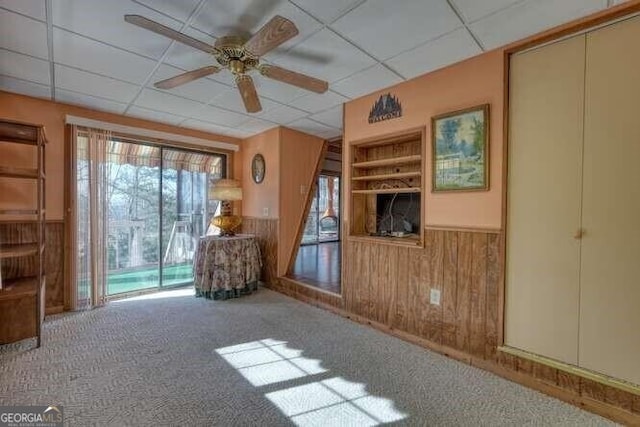 unfurnished room with carpet floors, wainscoting, ceiling fan, wooden walls, and a drop ceiling