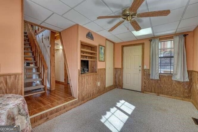 interior space featuring a paneled ceiling, a wainscoted wall, wooden walls, and stairs