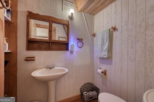 bathroom featuring toilet and wooden walls