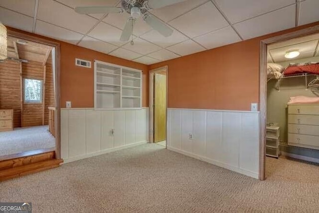 spare room with visible vents, a drop ceiling, a wainscoted wall, ceiling fan, and carpet