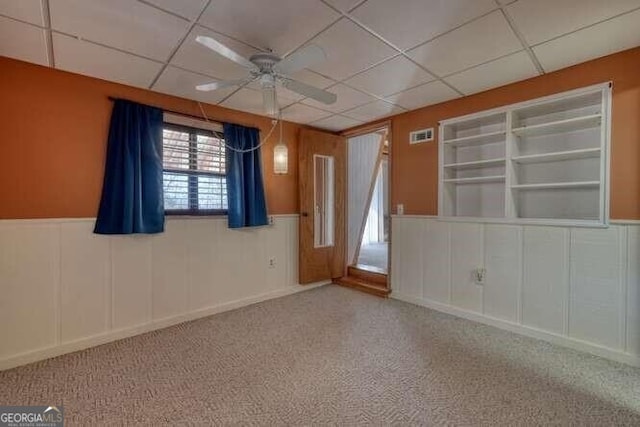 carpeted empty room with a paneled ceiling, a ceiling fan, and a decorative wall