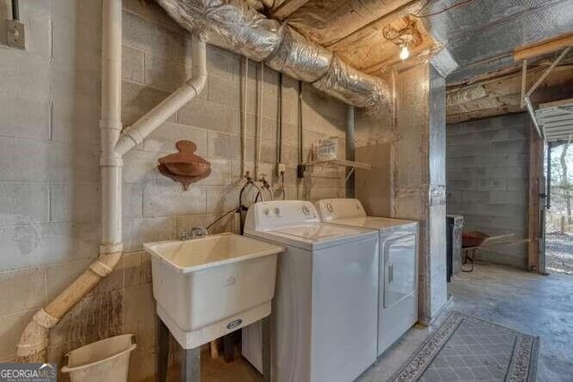 laundry area featuring concrete block wall, laundry area, a sink, and washing machine and clothes dryer