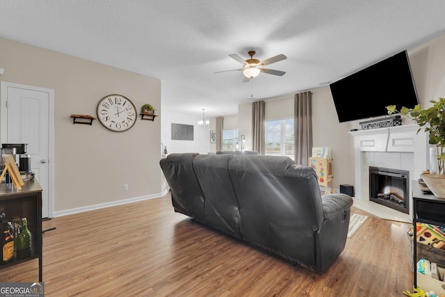 living room featuring a textured ceiling, ceiling fan with notable chandelier, light hardwood / wood-style floors, and a fireplace