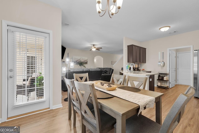 dining room featuring ceiling fan with notable chandelier and light hardwood / wood-style flooring