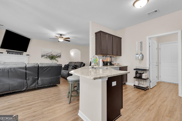 kitchen with dark brown cabinetry, ceiling fan, sink, light hardwood / wood-style floors, and a breakfast bar