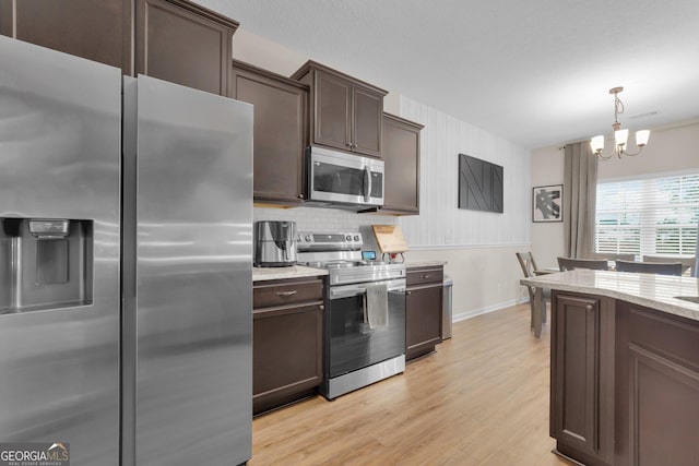 kitchen featuring dark brown cabinetry, hanging light fixtures, an inviting chandelier, light hardwood / wood-style floors, and appliances with stainless steel finishes