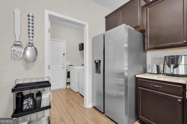 kitchen with stainless steel refrigerator with ice dispenser, decorative backsplash, light wood-type flooring, dark brown cabinetry, and washing machine and clothes dryer