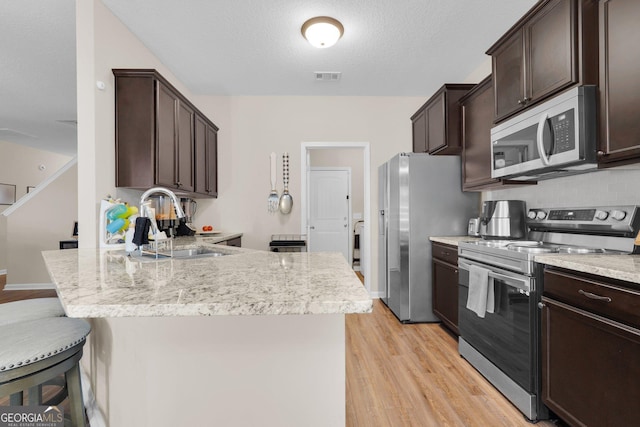 kitchen featuring dark brown cabinetry, sink, stainless steel appliances, light hardwood / wood-style floors, and a textured ceiling