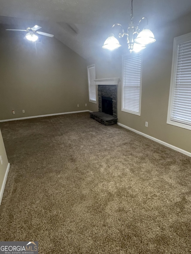 unfurnished living room with dark carpet, ceiling fan with notable chandelier, vaulted ceiling, and a stone fireplace