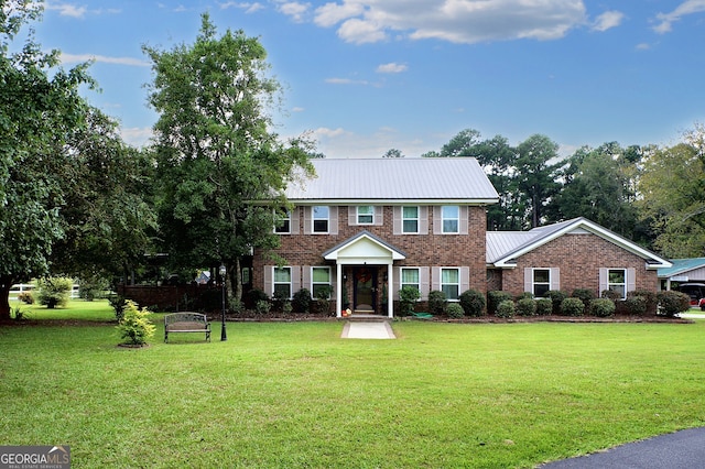 colonial house featuring metal roof, brick siding, a front yard, and a standing seam roof