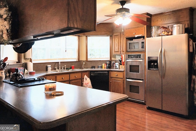 kitchen with a peninsula, wood finished floors, stainless steel appliances, a ceiling fan, and a sink