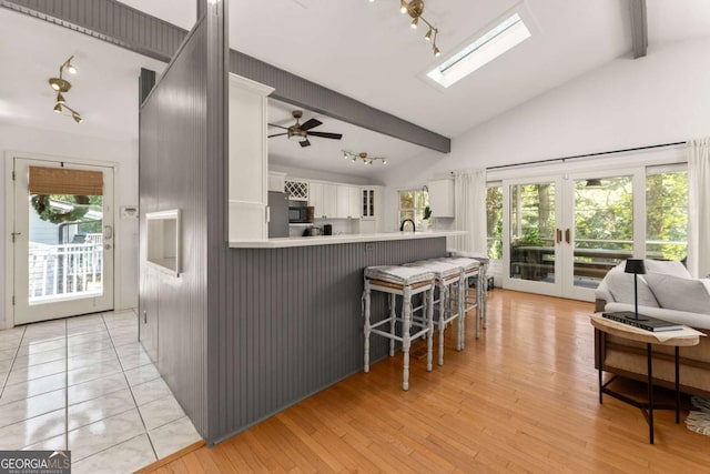 kitchen with kitchen peninsula, a skylight, a breakfast bar, ceiling fan, and white cabinetry