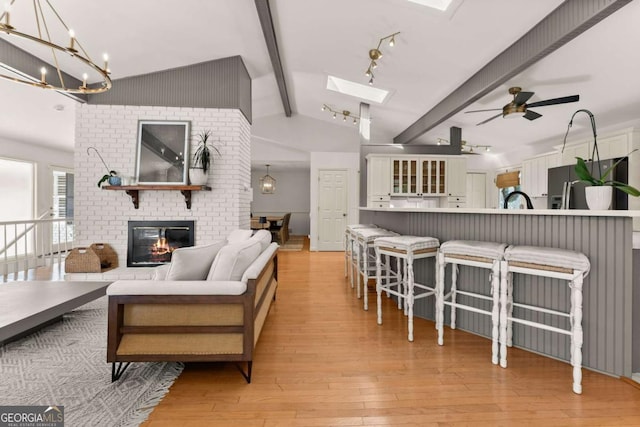 living room with light wood-type flooring, a brick fireplace, ceiling fan, and lofted ceiling with skylight