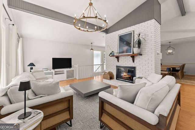 living room featuring vaulted ceiling with beams, light hardwood / wood-style flooring, and a brick fireplace