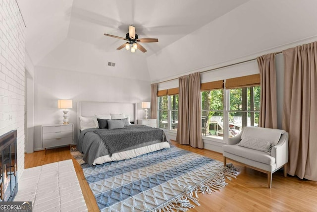 bedroom with a brick fireplace, a raised ceiling, ceiling fan, high vaulted ceiling, and hardwood / wood-style floors