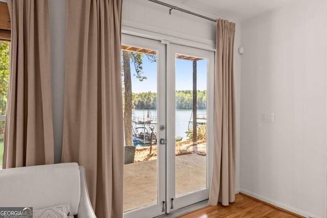 entryway with french doors, a water view, a wealth of natural light, and hardwood / wood-style floors