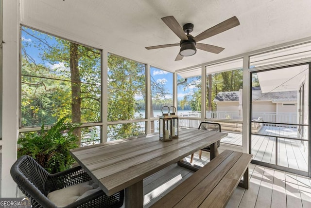 sunroom with ceiling fan and a water view