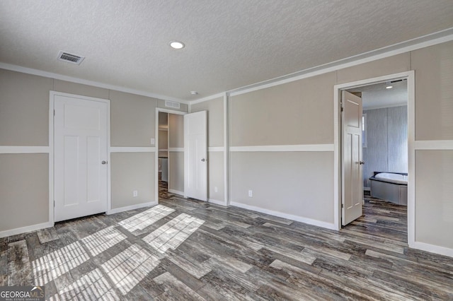 unfurnished bedroom with a textured ceiling, ensuite bathroom, dark hardwood / wood-style flooring, and crown molding