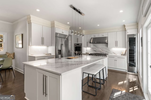 kitchen featuring a sink, under cabinet range hood, ornamental molding, high end fridge, and dark wood-style flooring