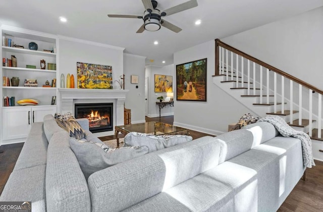 living room featuring built in shelves, ceiling fan, dark hardwood / wood-style flooring, and ornamental molding