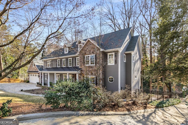 view of front of home featuring a garage, fence, stone siding, and driveway